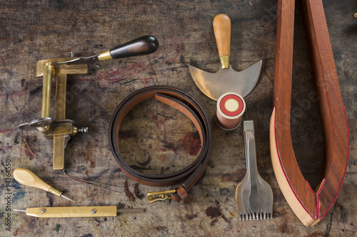 Leather goods craftsman's tools and a ready belt on a dirty work bench
