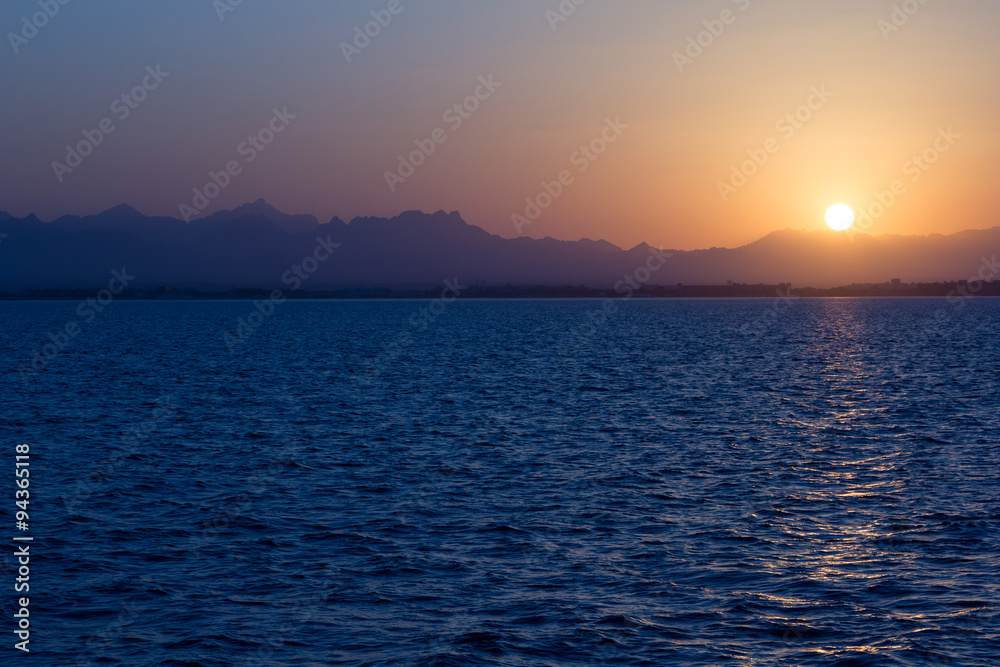 Sonnenuntergang vom Meer aus, im Hintergrund sind Berge zu sehen