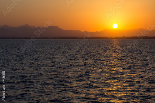 Sonnenuntergang vom Meer aus, im Hintergrund sind Berge zu sehen