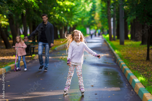 Little girl with father and sister in roller skates at a park