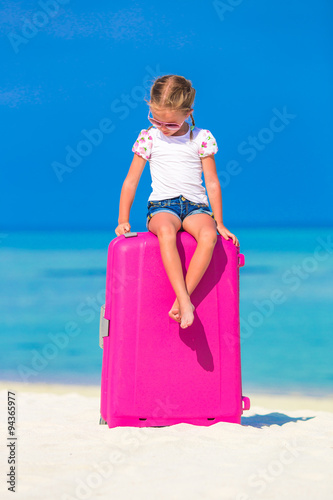 Little adorable girl with big luggage on tropical island 