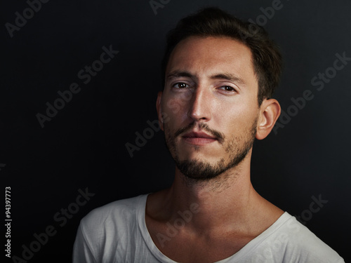 Portrait of cute young man wearing white tshirt and looks serious. Horizontal