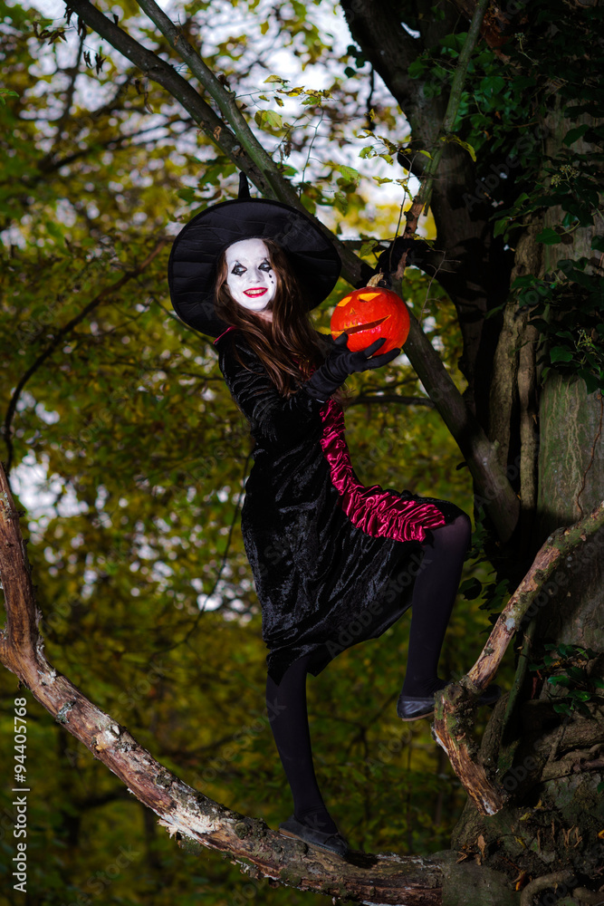 Teenage girl dressed in witch costume sitting on the tree