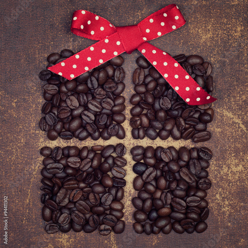 A red ribbon bow on top of a dark roasted coffee beans present o