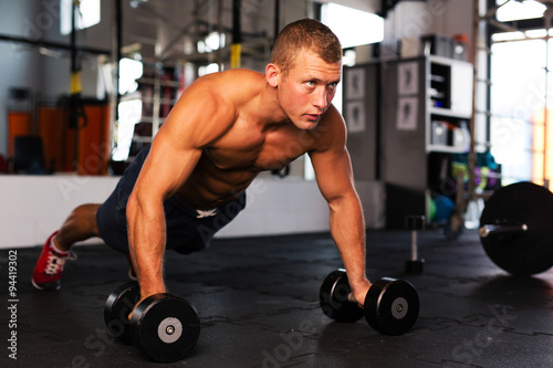 Young man doing pushups on dumbbells at gym