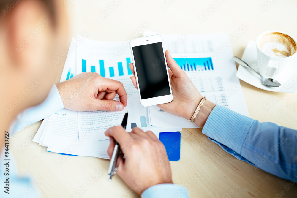 Fototapeta premium Close-up of a female hand holding a white smartphone during business meeting