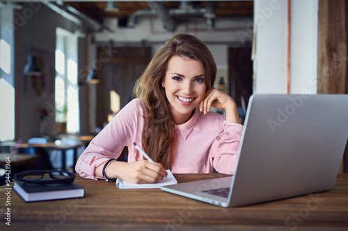 Happy female student at cafe with laptop and notepad