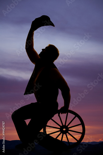silhouette cowboy sitting on wagon wheel hold hat up