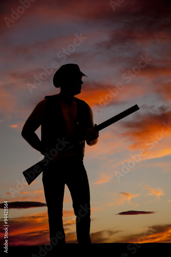 silhouette of cowboy with shotgun by waist in sunset