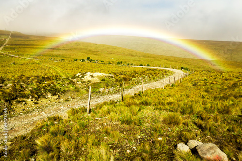 Experience the breathtaking beauty of a high altitude road adorned with a vibrant rainbow,nestled amidst the majestic Andes Mountains.