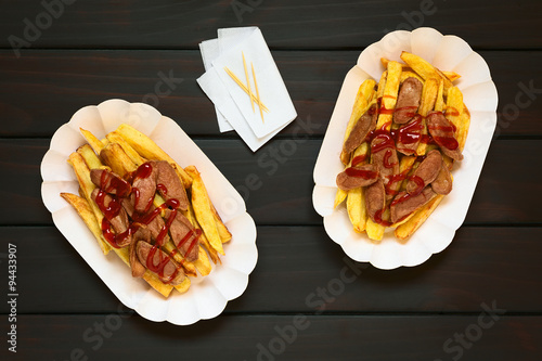 Salchipapas made of French fries and fried sausage, a traditional fast food in South America, photographed overhead on dark wood with natural light