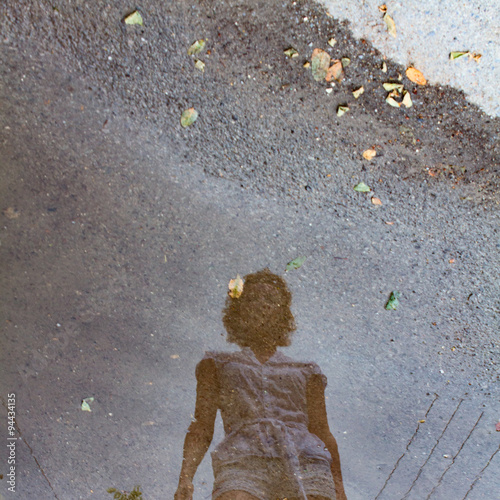 a reflection of a young girl in a puddle after rain.