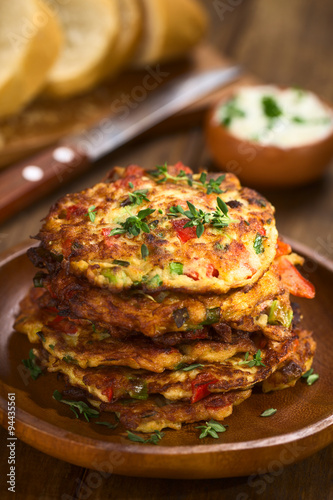 Vegetable and egg fritter made of zucchini  red bell pepper  eggs  green onions and thyme piled on a wooden plate  Selective Focus  Focus on the front of the thyme sprig on the top of the fritters 