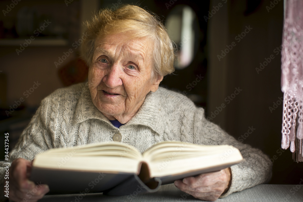 An elderly woman with a book sitting at the table. An elderly woman with a book sitting at the table.