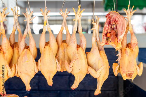 A raw, fresh Ecuadorian chicken hanging by a hook in a poultry market, waiting for processing and sale.