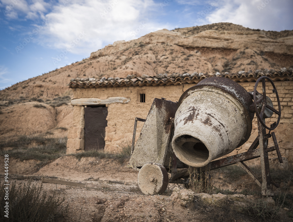 A rusty brown Cement Mixer and an old house 