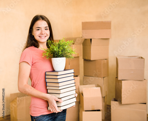 Young woman moving house to college, holding pile books and plan photo