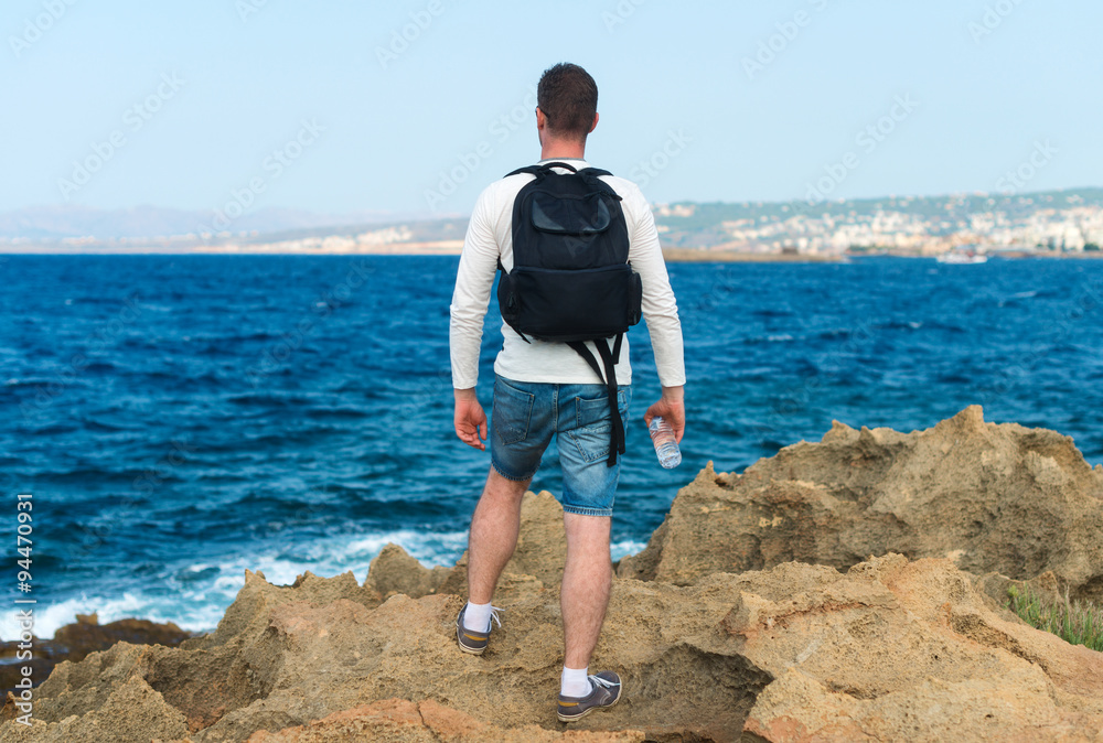 Male tourist with backpack standing near the sea. Place for your text.