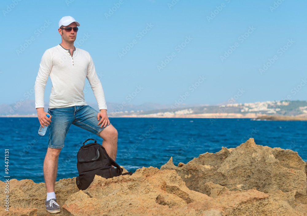 Male tourist with backpack standing near the sea. Place for your text.