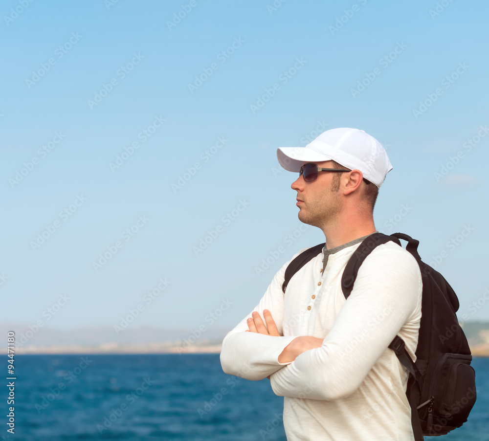 Male tourist with backpack standing near the sea. Male tourist with backpack standing near the sea.