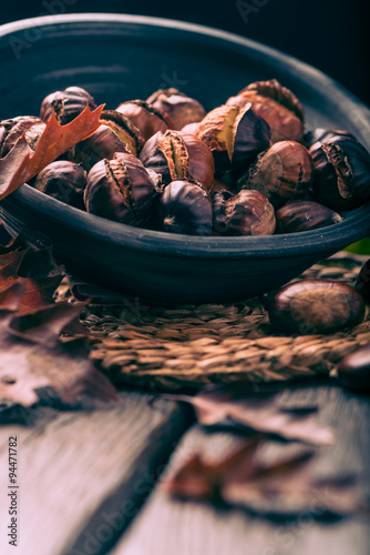 Roasted chestnuts on a rustic wooden table with autumn leaves in the background. photo