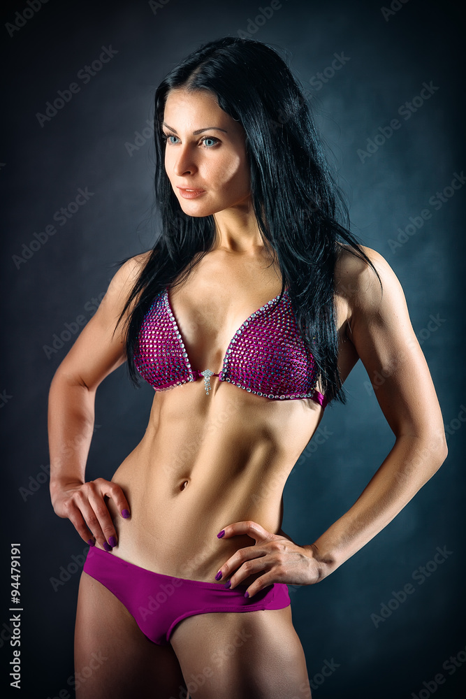 Muscular young woman athlete portrait over dark background