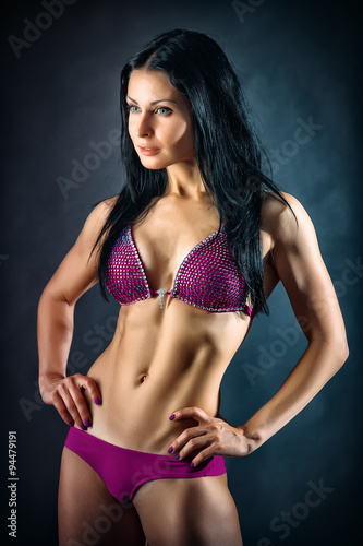 Muscular young woman athlete portrait over dark background