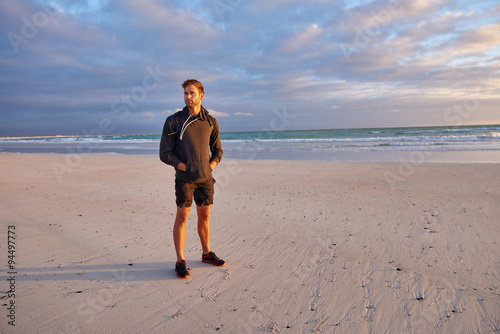 Fit young man standing on a beach at sunrise