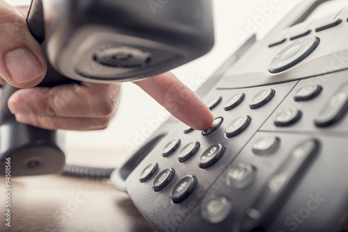 Closeup of male hand holding telephone receiver while dialing a photo