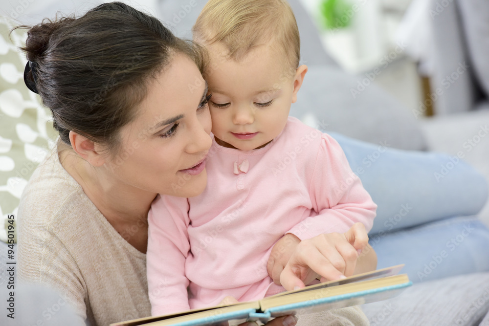 Mother and daughter reading book sitting in sofa Mother and daughter reading book sitting in sofa