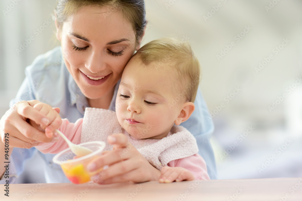 Young mother helping baby girl with eating by herself Young mother helping baby girl with eating by herself
