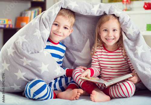 Happy siblings reading book under cover