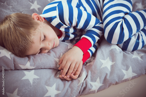 Cute little boy sleeps in pajames on bed. Fokus above photo