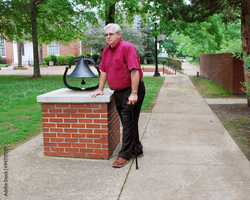 Elderly Man With Cane Standing Beside a Bell in the Park