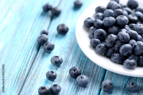 Tasty blueberries in plate on a blue wooden table