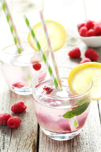 Raspberries and juice in glass on grey wooden background