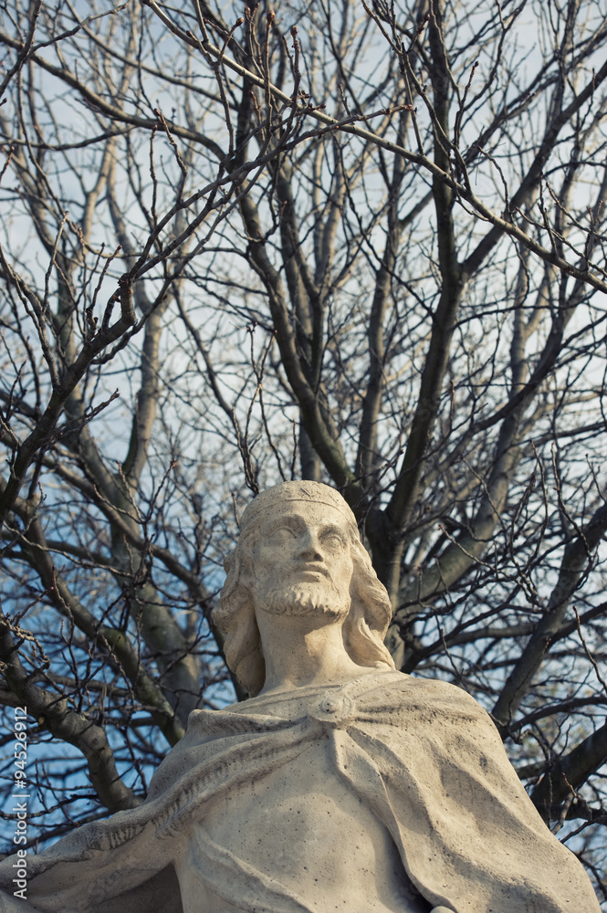 statue's close view behind bare trees in retiro's park in madrid statue's close view behind bare trees in retiro's park in madrid
