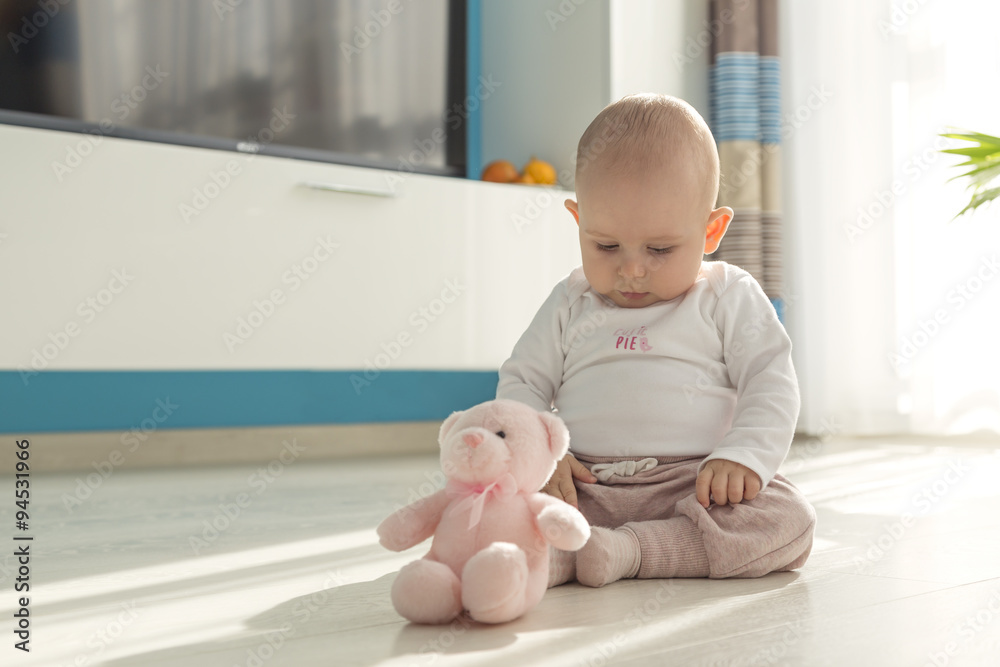 baby sitting in sunny living room on the ground and playing with teddy bear baby sitting in sunny living room on the ground and playing with teddy bear