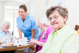 Gruppe Senioren isst in Kantine von Altenheim, eine Pflegerin serviert
