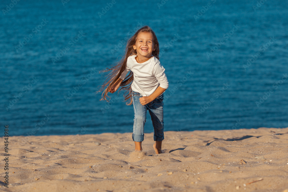Adorable happy smiling little girl on beach vacation. jeans.