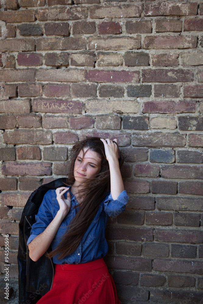 Young, pale, thoughtful, solitude ,smiling girl with long brown hair and a birthmark on face leaning against the brick wall wearing jeans blue shirt and holding a black jacket Young, pale, thoughtful, solitude ,smiling girl with long brown hair and a birthmark on face leaning against the brick wall wearing jeans blue shirt and holding a black jacket