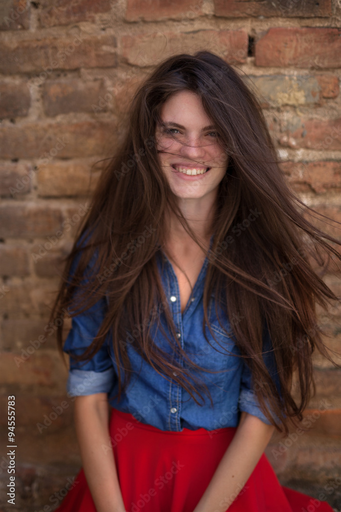 portrait of young, youth, cheerful, prettysmileing girl with long brown hair beside brick wall wearing jeans blue shirt and red scirt portrait of young, youth, cheerful, prettysmileing girl with long brown hair beside brick wall wearing jeans blue shirt and red scirt