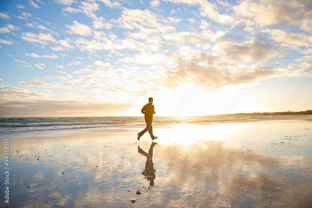 Man running on the beach with clouds and sun flare