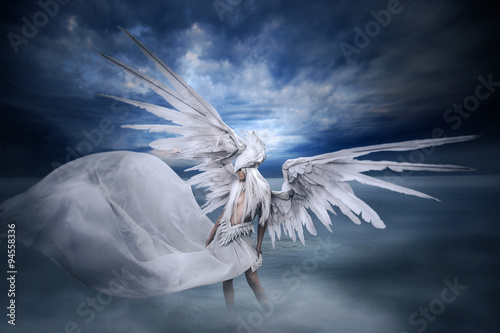 young girl with  big white wings, standing in the lake in landscape with dramatic sky and fog. photo