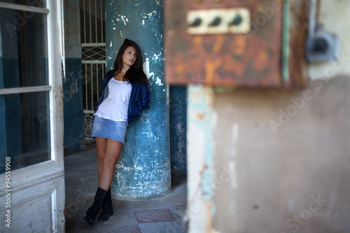 Fashion ,young pretty,girl with dark hair, with blue shiny jacket and jeans mini skirt with boots, standing in old building,thoughtful,thinking, leaning on the big blue old pillar  © Marko Stamatovic