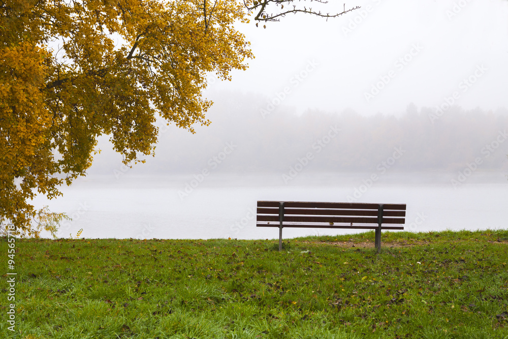 Rising mist over peaceful lake with solitary empty park bench and autumn tree on left. Rising mist over peaceful lake with solitary empty park bench and autumn tree on left.