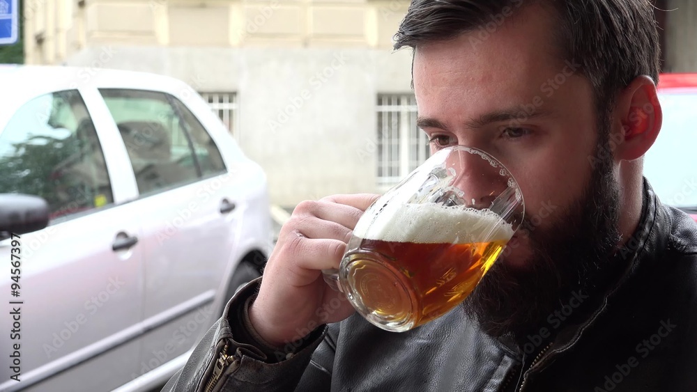 young handsome hipster man drinks beer in the restaurant - outside seating - street with people and parked car young handsome hipster man drinks beer in the restaurant - outside seating - street with people and parked car