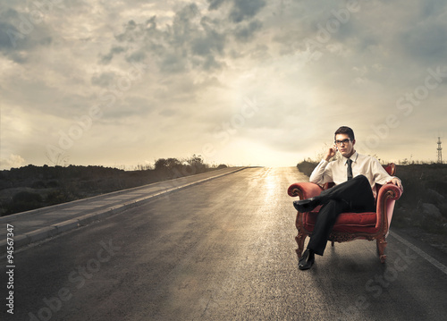 Businessman sitting in red chair in a solitary road in the countryside