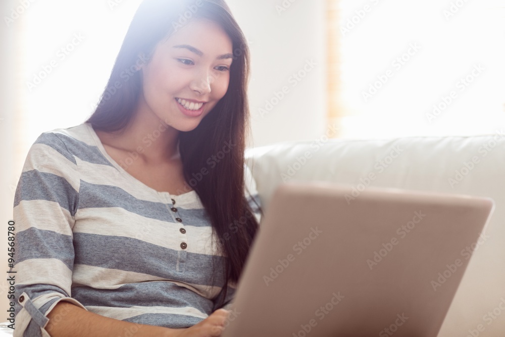 Smiling asian woman using laptop on couch Smiling asian woman using laptop on couch