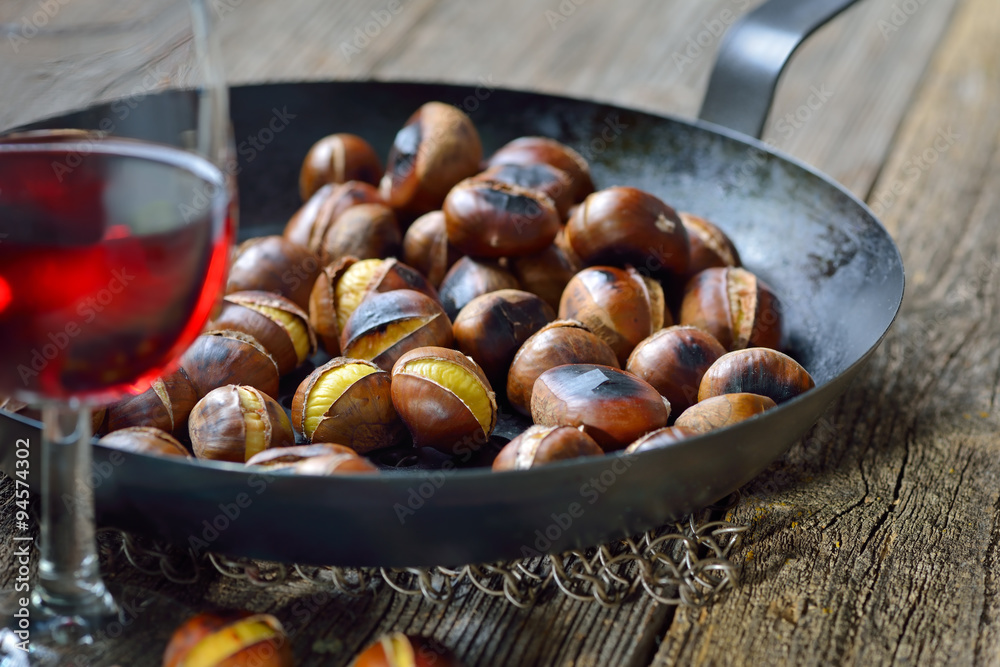 Pfanne mit frisch gerösteten Maronen. mit einem Glas Vernatsch zum Törggelen in Südtirol serviert Pfanne mit frisch gerösteten Maronen. mit einem Glas Vernatsch zum Törggelen in Südtirol serviert